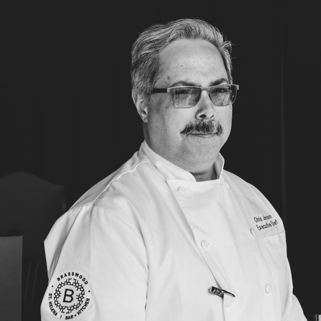 An photo of Brasswood Executive Chef, Chris Johnson, wearing a white chef's garment with a Brasswood logo on the sleeve.