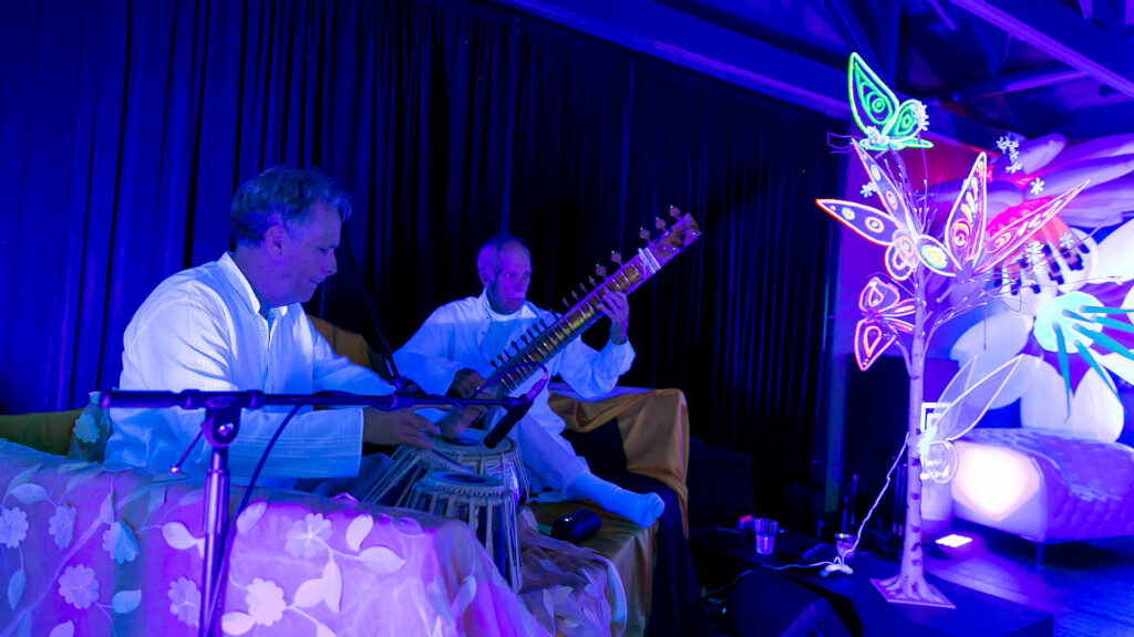 A photo of 2 musicians performing in the Brasswood event space as part of a performance for the BudBreak event in a black lit room.