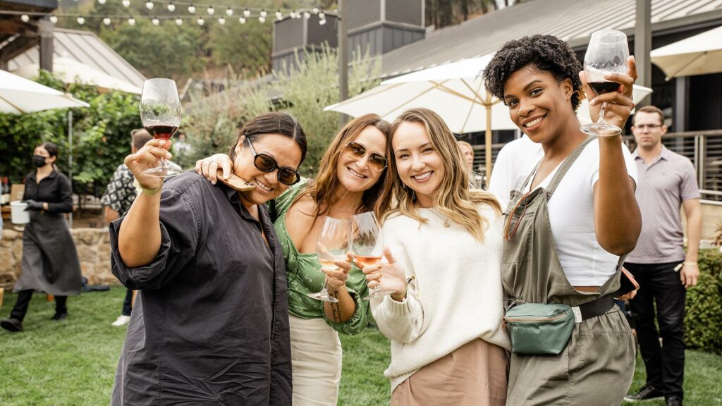 An image of a group of 4 diverse women, posing for a picture at Brasswood Estate, with wine in their hands, appearing jovial.