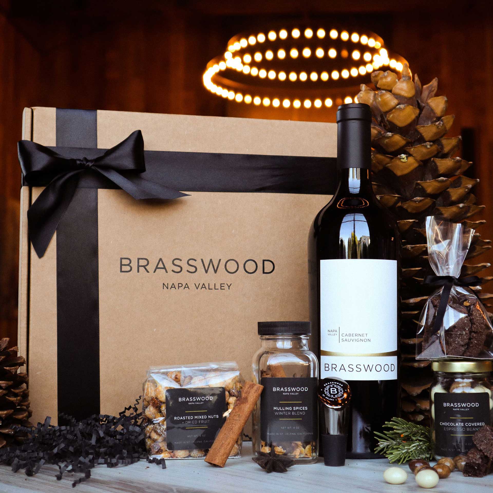 A photograph of the Brasswood holiday winter box with Cabernet Sauvignon, and other gift accessories in glass jars and vacuum-sealed snacks.