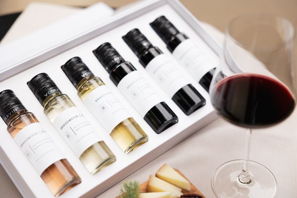 A wine sampler gift box, featuring 6 different wine samples and a glass of red wine from Brasswood, bottled in partnership with Coravin Vinitas.